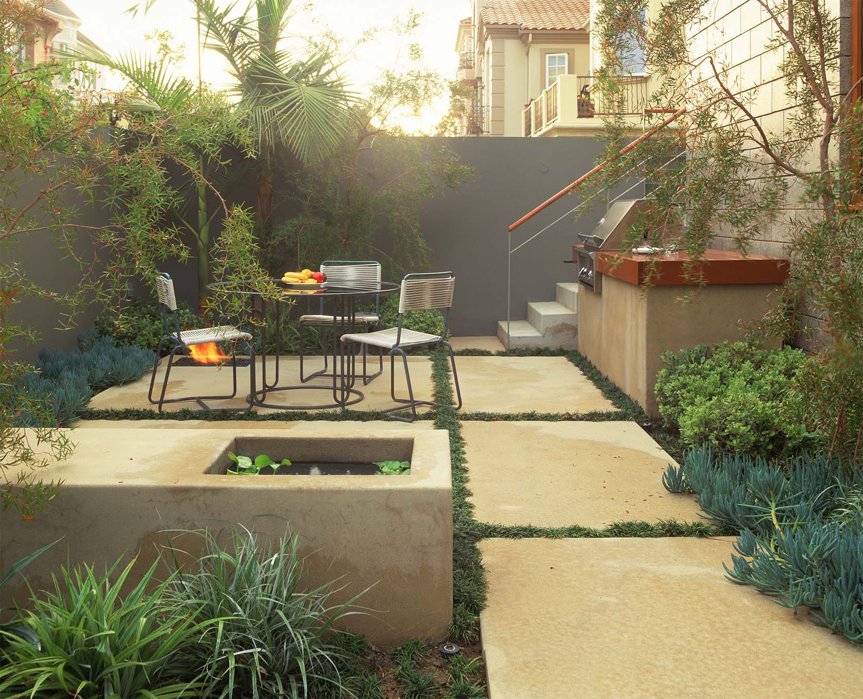 Small-space garden: Concrete pavers, a fountain with a miniature water garden, and a built-in barbecue anchor the space. The grill’s countertop ties in architectural detail.